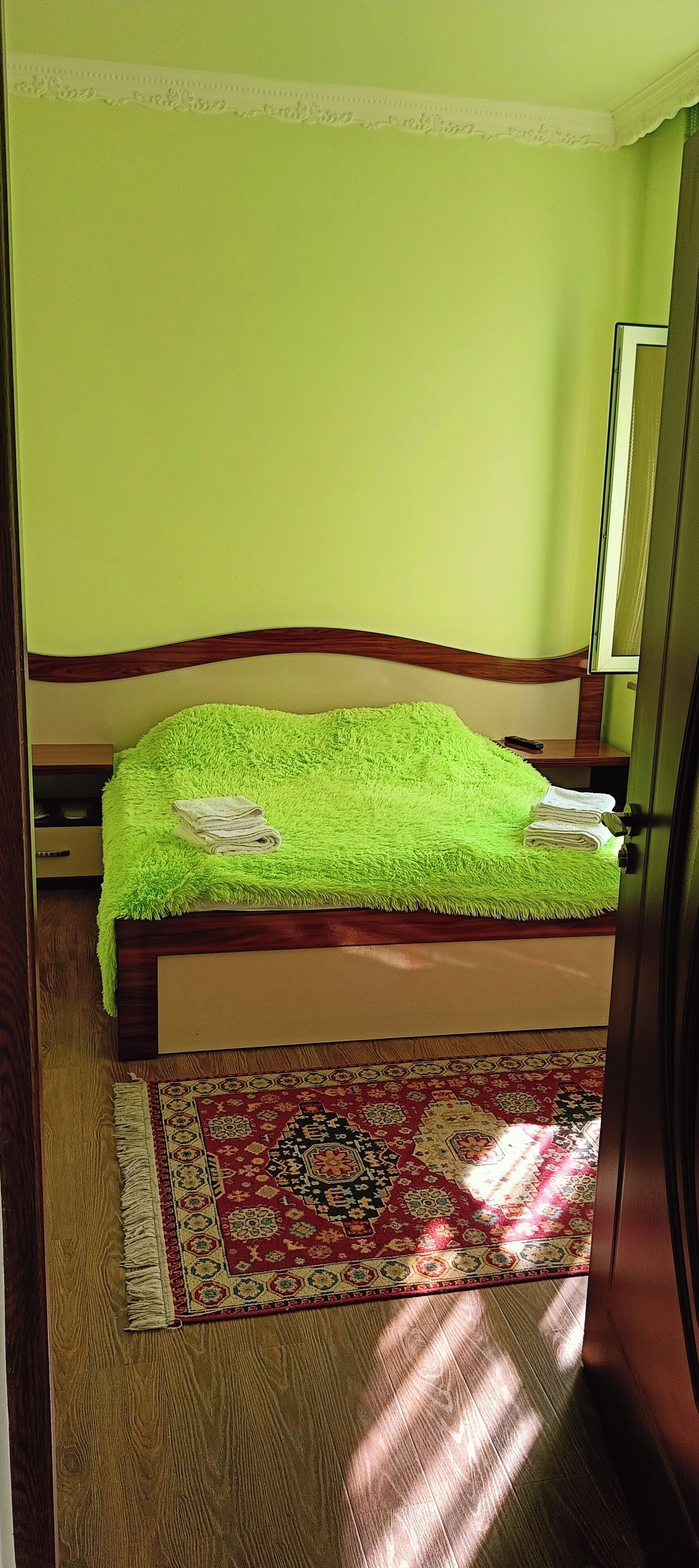 A room with a bed, a wooden floor, a patterned rug, and a green wall.