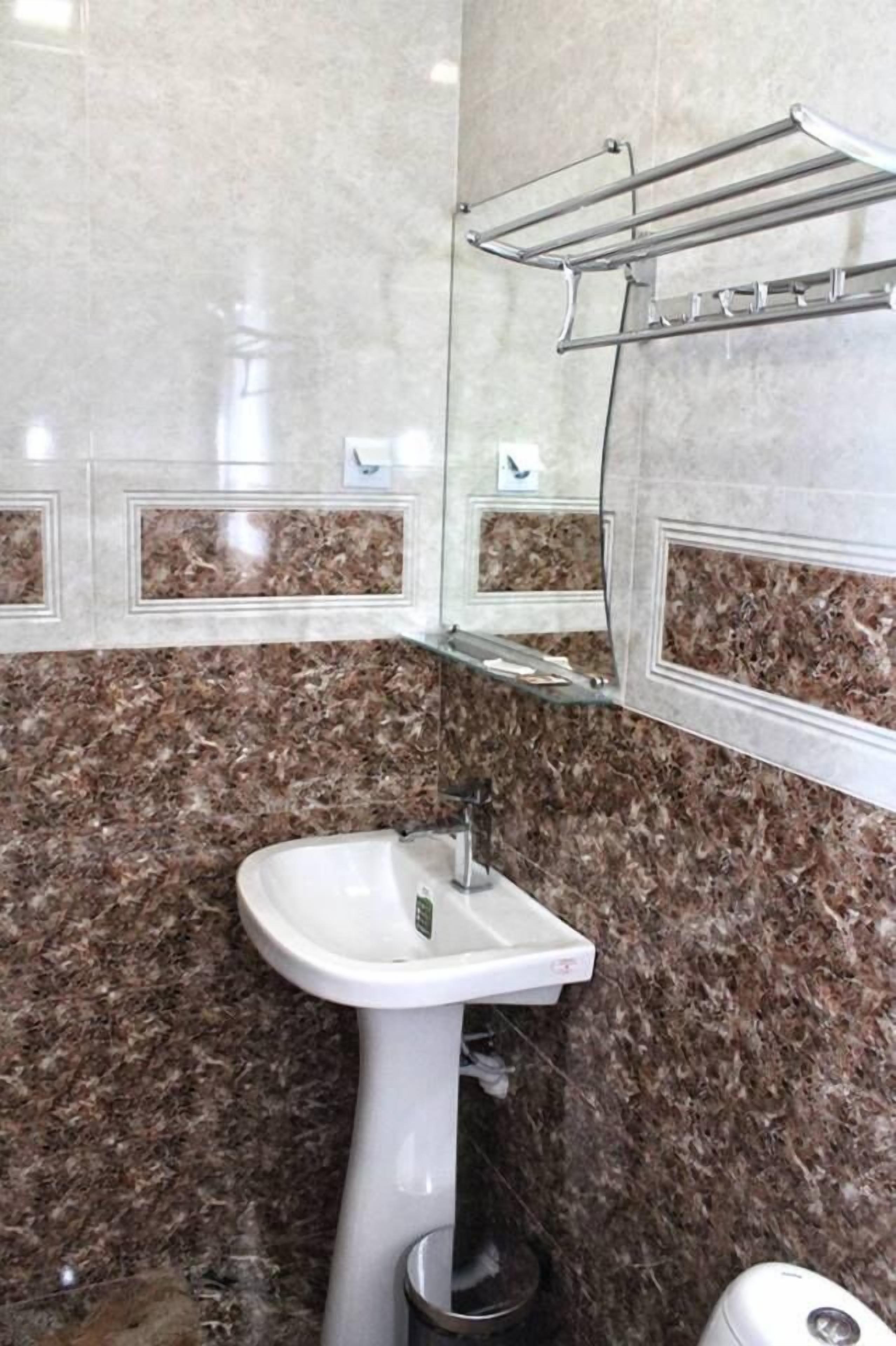 Casa de banho com lavatório branco, parede com padrão marmorizado e uma prateleira de vidro sobre o lavatório.