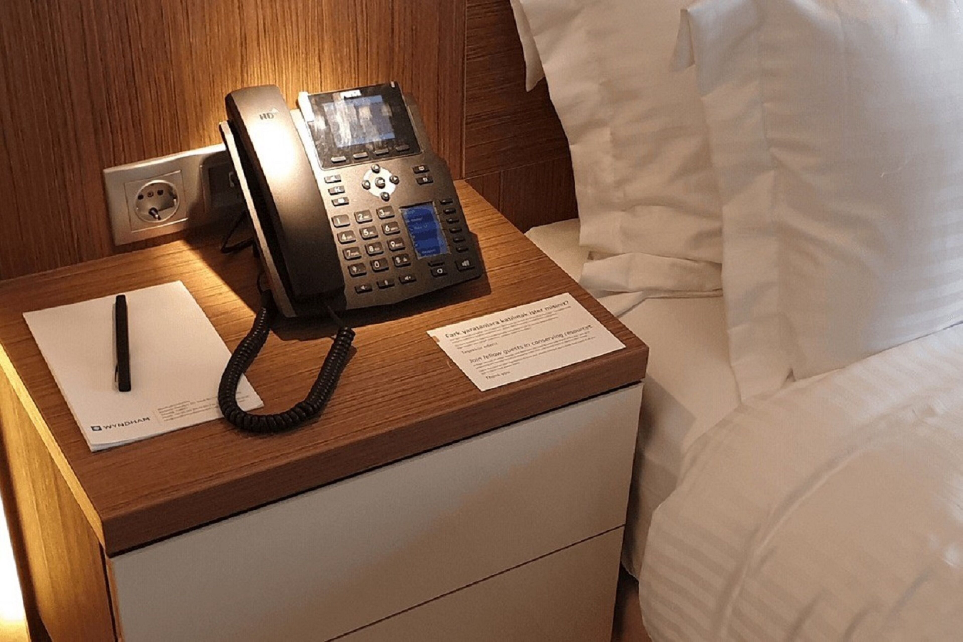 Une chambre d’hôtel avec une table de chevet en bois, un téléphone, un bloc-notes et un stylo.