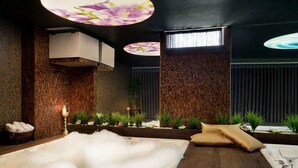 A spa room with a large hot tub, wooden walls, and decorative plants.