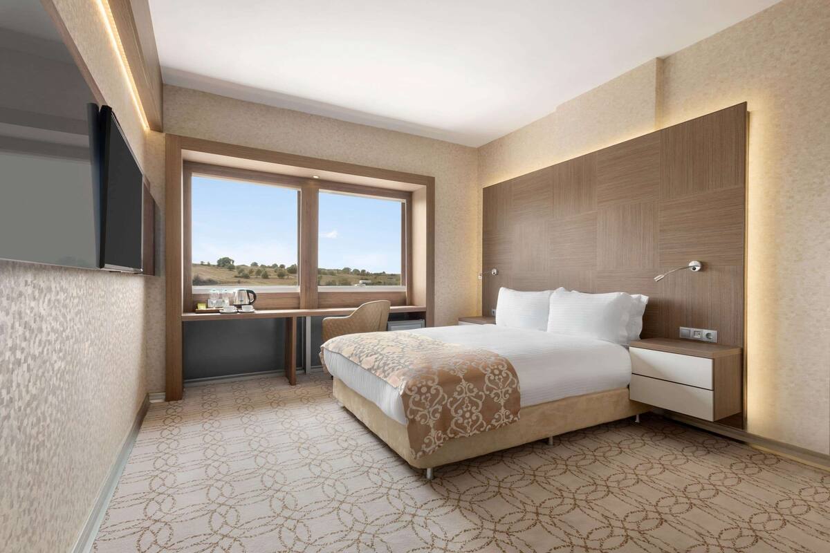 A modern hotel room with a large bed, a desk, and a view of the countryside.