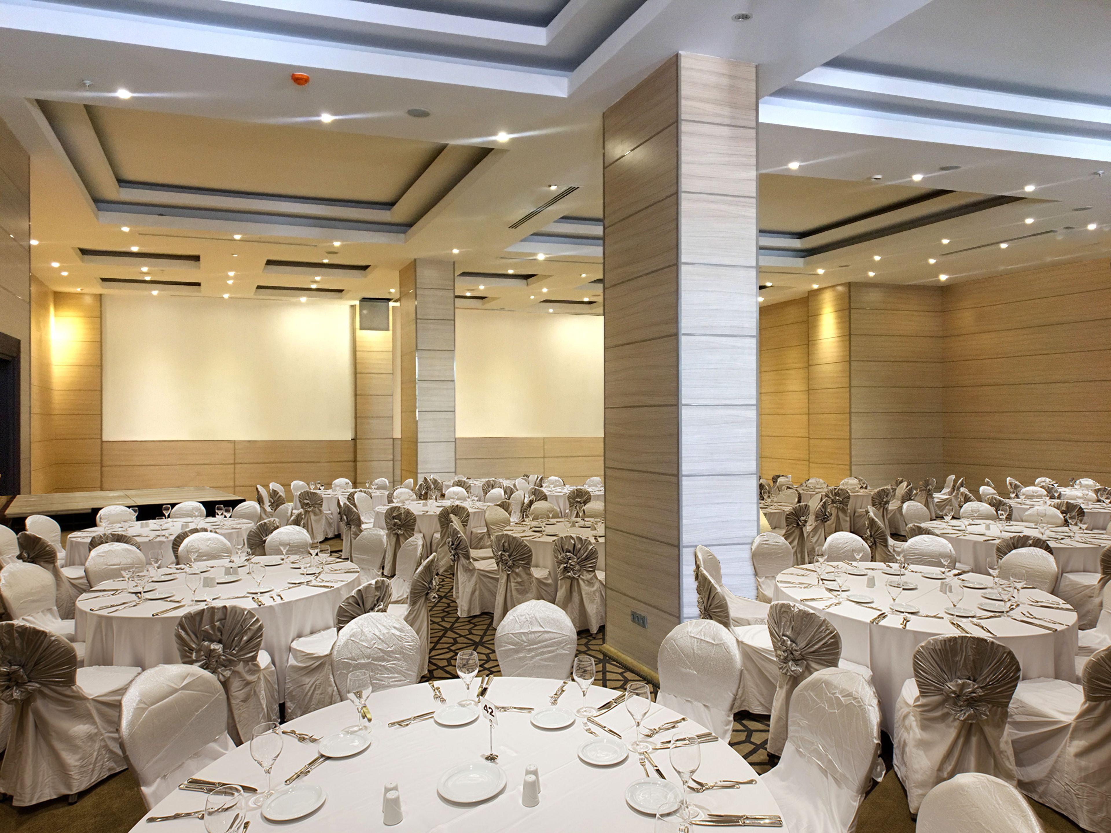 A large banquet hall with round tables set for a formal event, featuring white tablecloths and chairs with decorative sashes.