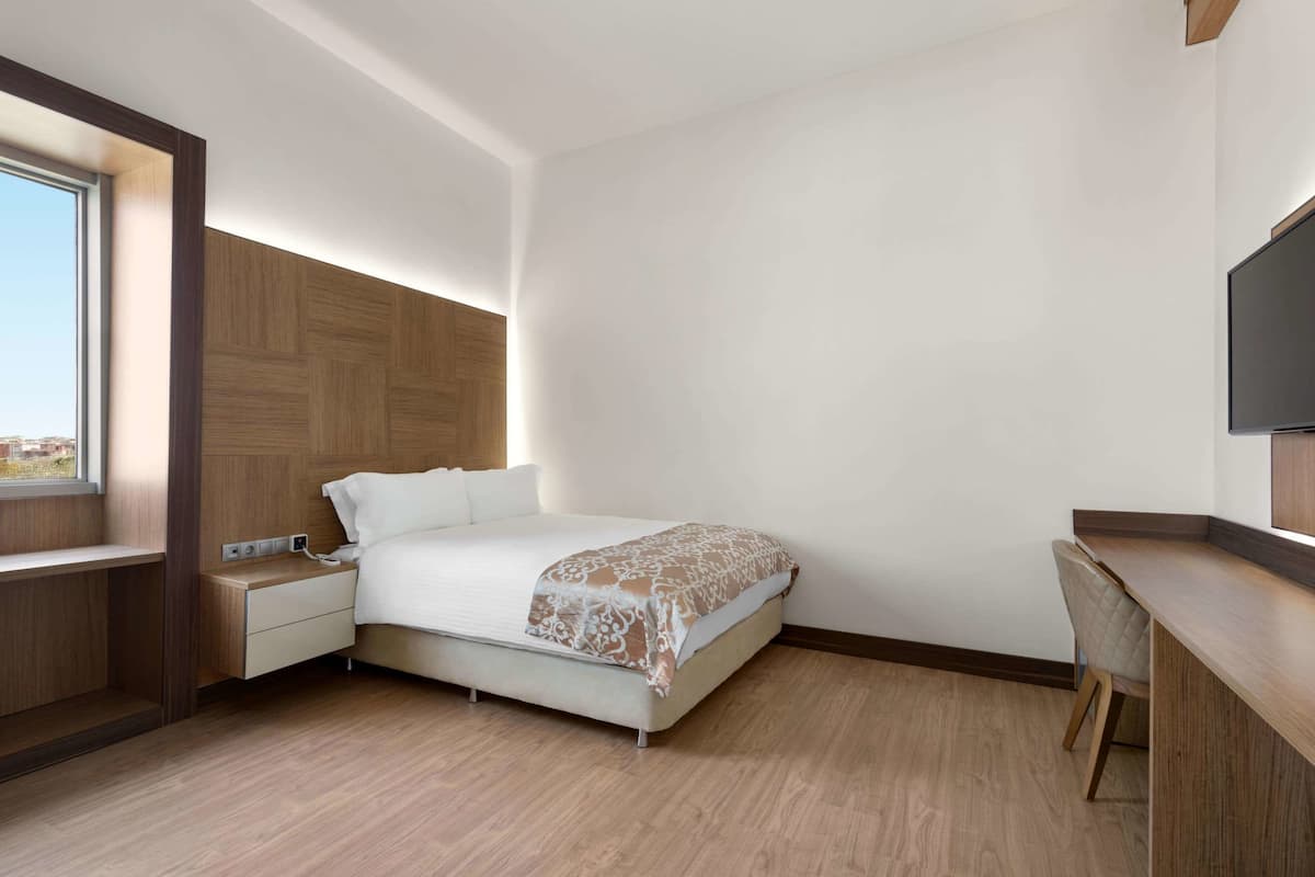 A modern hotel room with a bed, bedside table, and a desk area.
