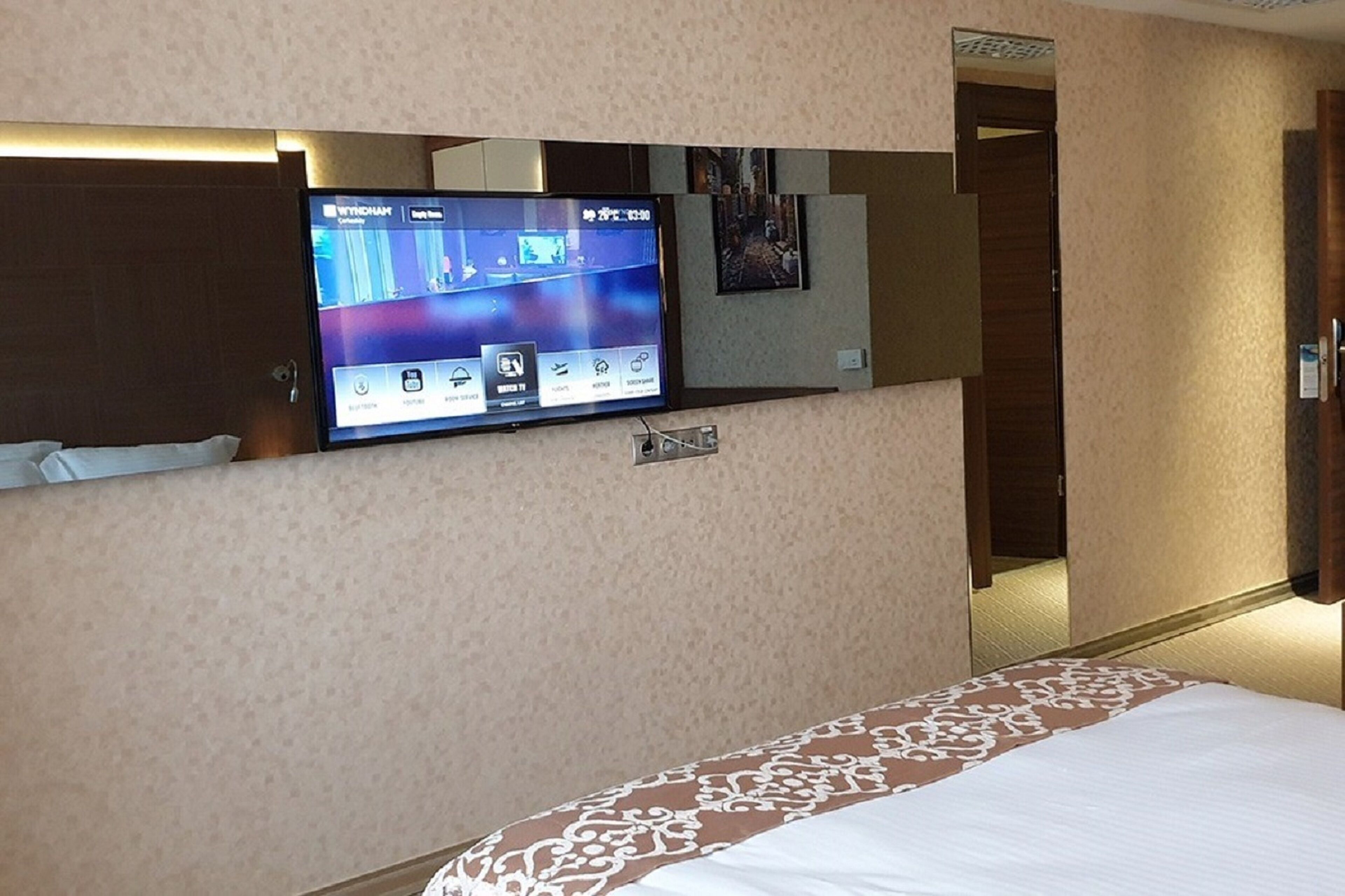 A hotel room with a bed, a television mounted on the wall, and a door leading to another room.