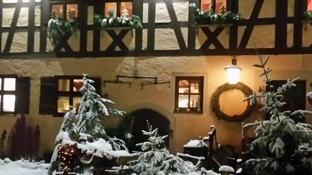 A building with a traditional half-timbered facade, a snow-covered courtyard, and a lit Christmas wreath.
