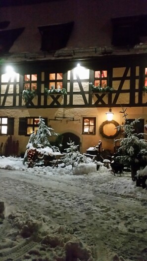 Un edificio con fachada de entramado tradicional, un patio cubierto de nieve y un adorno navideño iluminado.