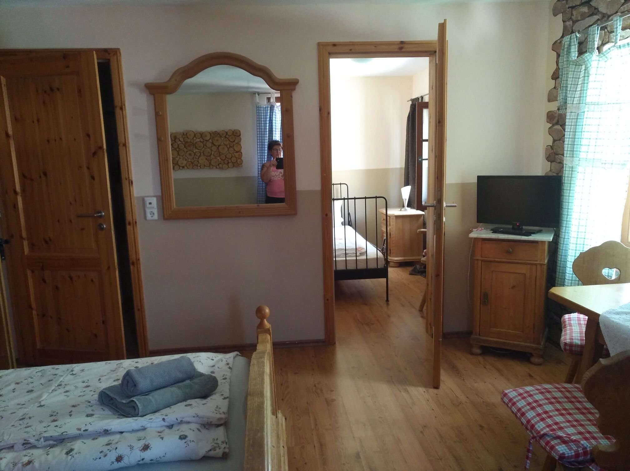 A bedroom with a wooden bed, a bedside table, a mirror, a wardrobe, and a television.