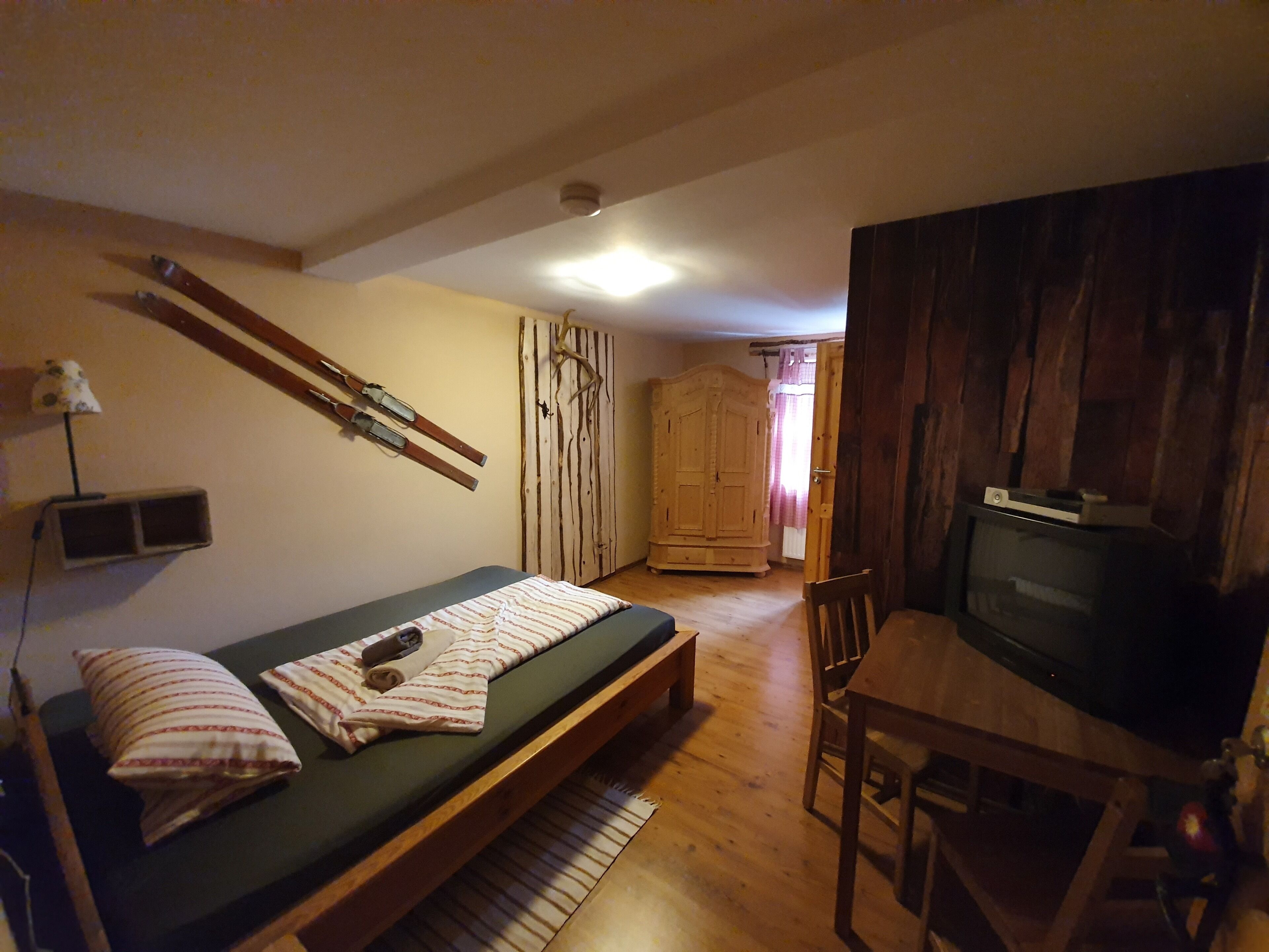 Een kleine kamer met een bed, een televisie, een houten garderobe en een paar ski's die tegen de muur staan.