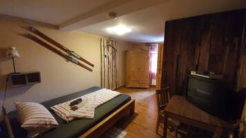 Een kleine kamer met een bed, een televisie, een houten garderobe en een paar ski's die tegen de muur staan.