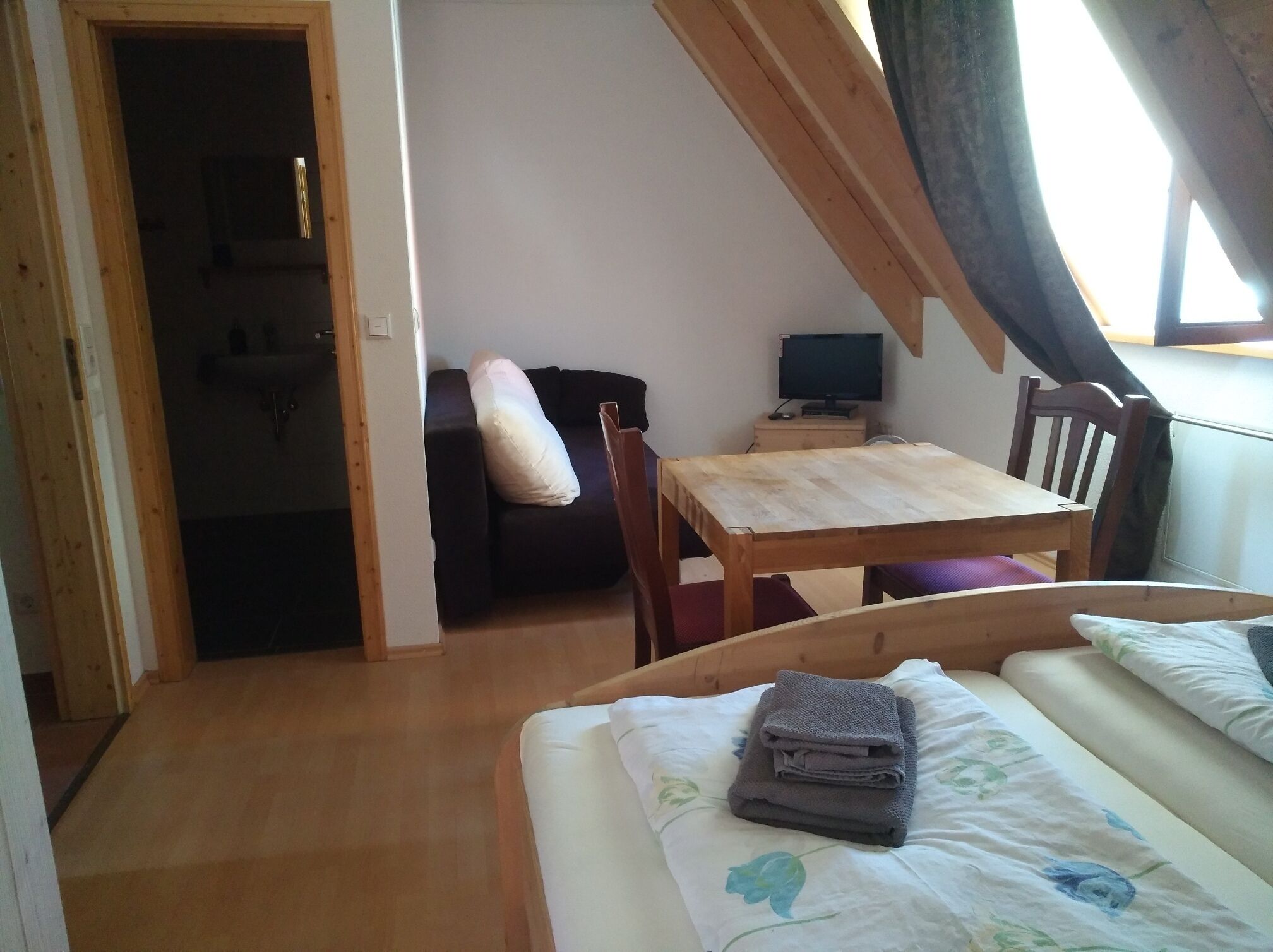 Ein Schlafzimmer mit einem Holzbett, einem kleinen Tisch, einem Stuhl, einer Couch und einem Fernseher im Hintergrund.
