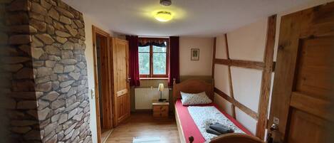Un pasillo estrecho que conduce a un dormitorio con una cama de madera, pared de piedra y una ventana con cortinas rojas.