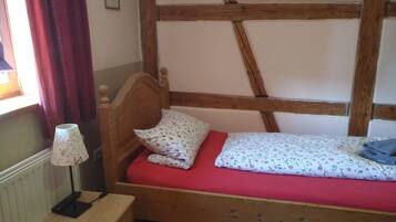 A small, single-bed room with a wooden headboard, a red mattress, and a bedside table with a lamp.