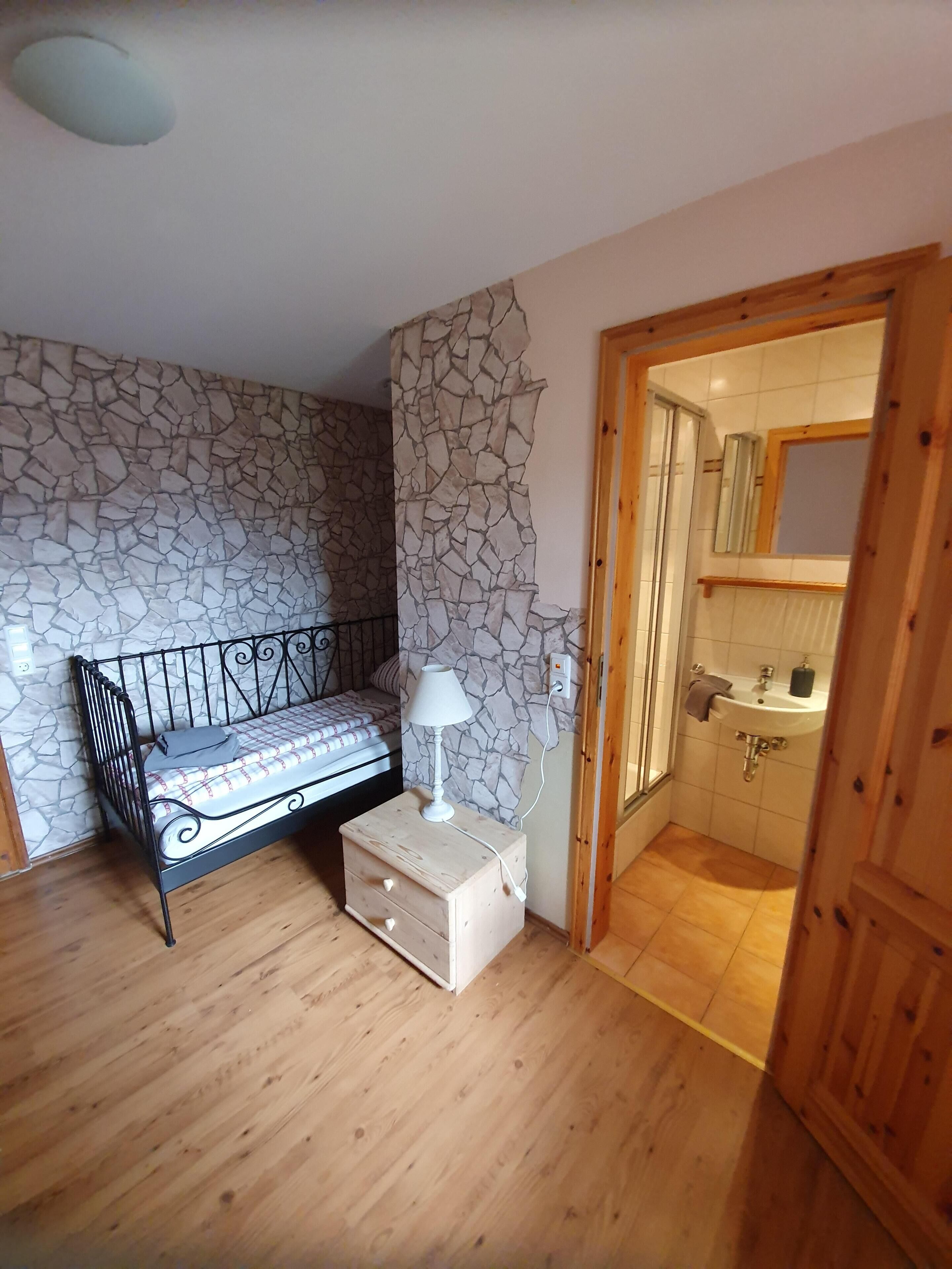 Une chambre à coucher comprenant un lit, une table de chevet, une lampe, ainsi qu’une salle de bain avec un lavabo et un miroir.