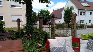 A wooden bench with cushions, a wooden fence, and a wheelbarrow in a garden setting.