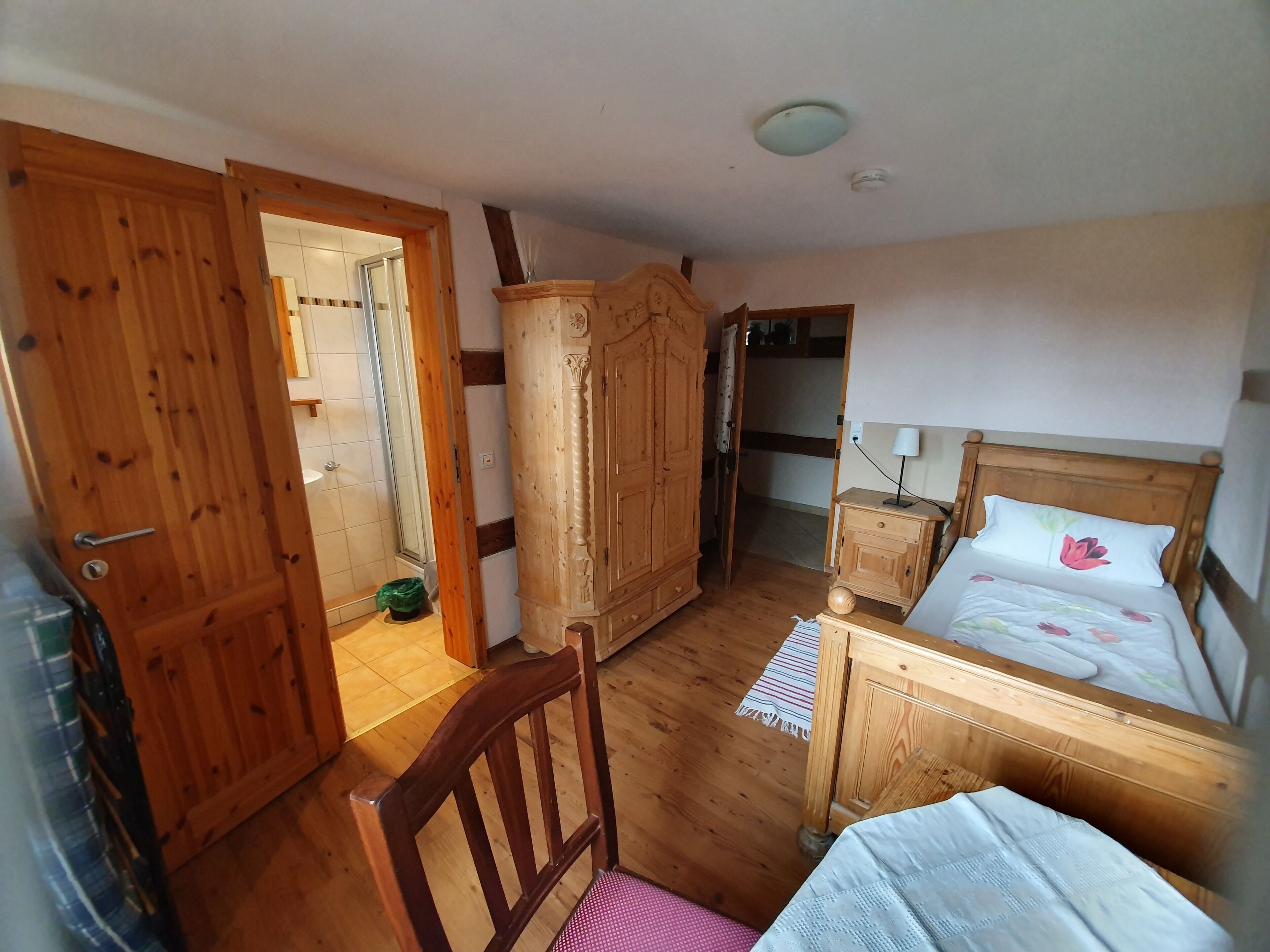 Un dormitorio con cama de madera, un armario de madera, una silla de madera y una mesita de noche pequeña con una lámpara.