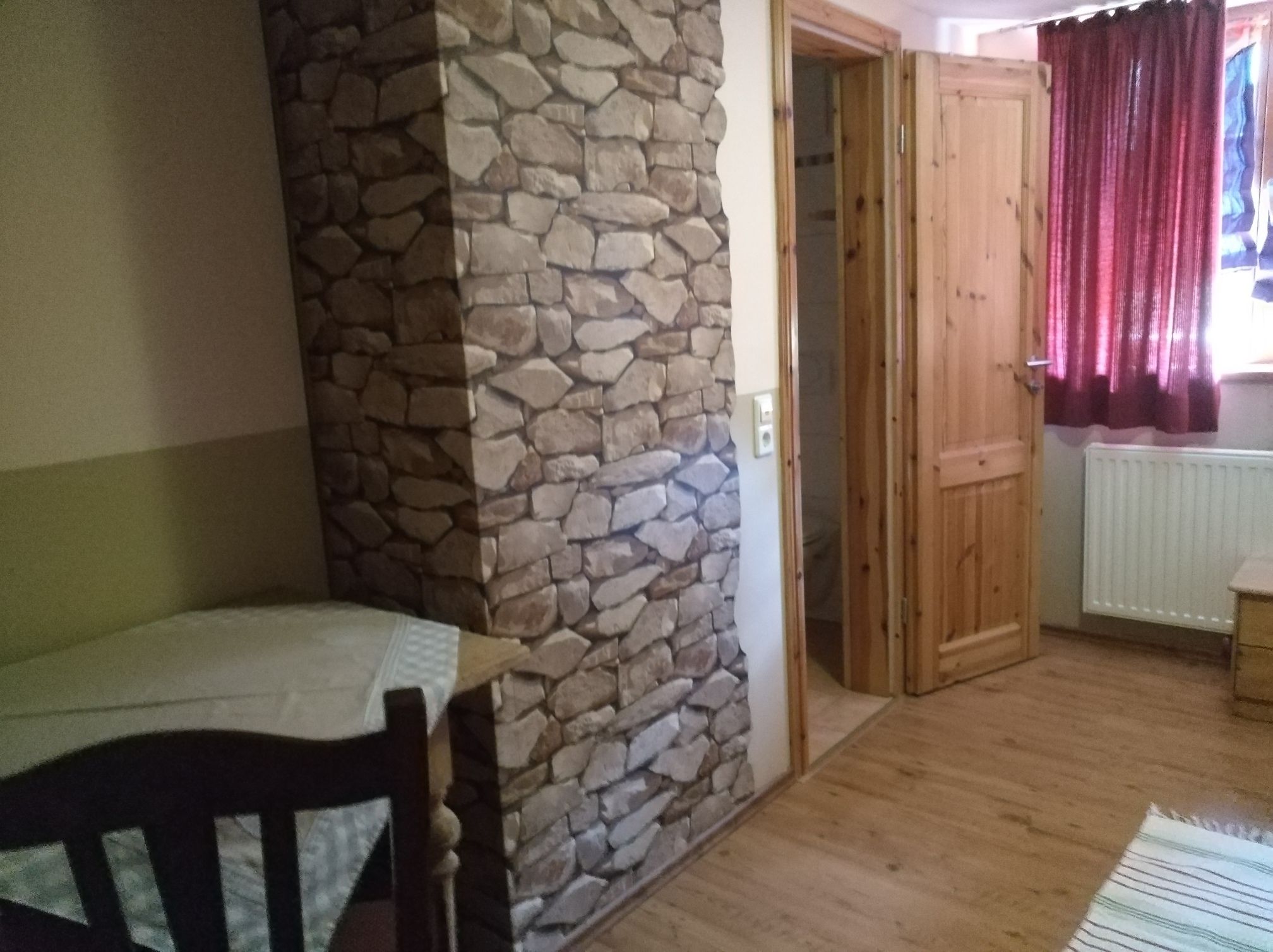 A room with a stone wall, wooden door, and a table with a chair.