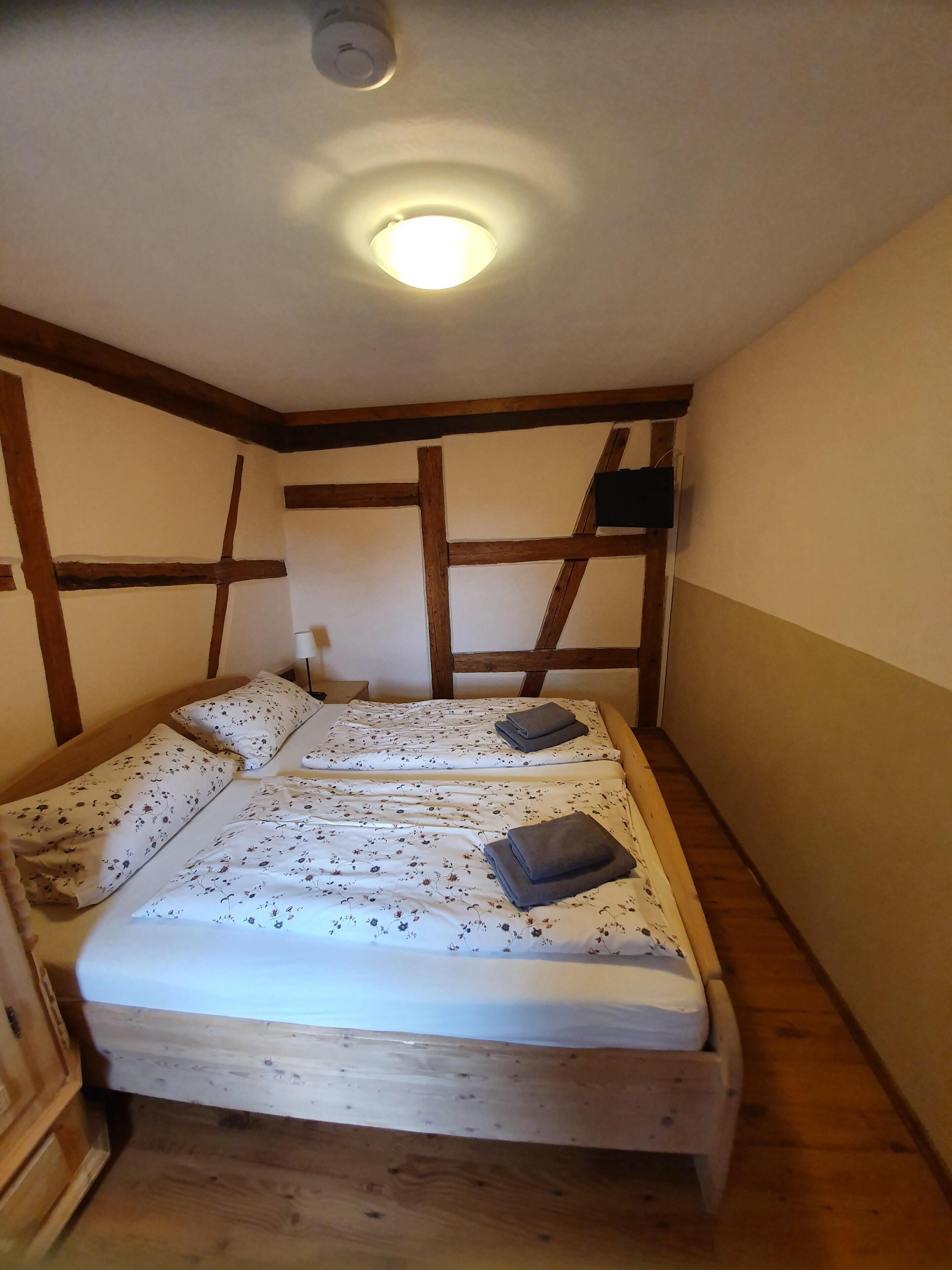 Una habitación pequeña y acogedora con una cama individual, vigas de madera en las paredes y una lámpara en el techo.