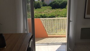 A room with a wooden table and chairs, a sliding glass door leading to a balcony with a view of greenery and buildings. - Housing near downtown (Montpellier)
