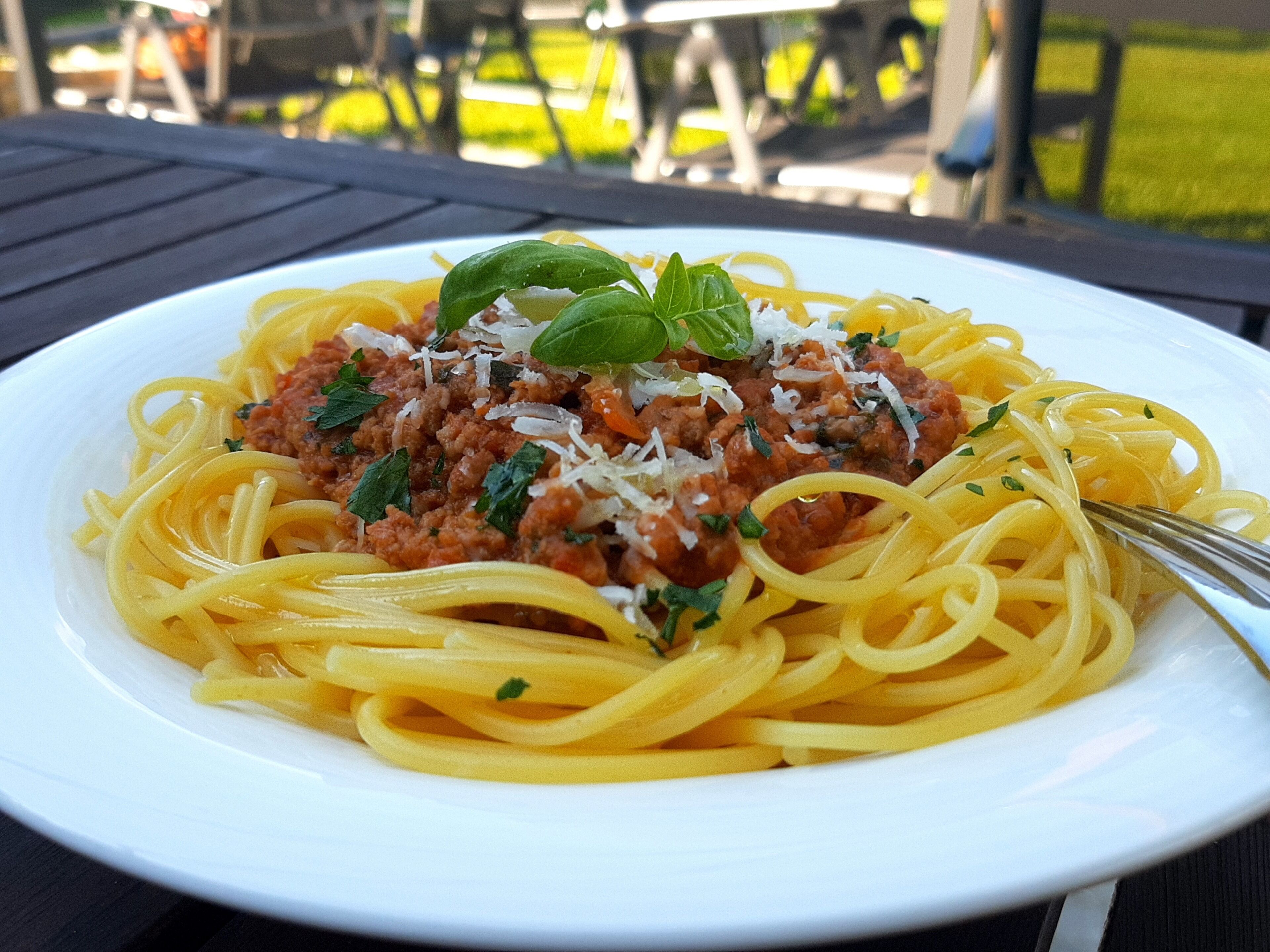 A plate of spaghetti with meat sauce and cheese, garnished with basil, on a white plate.