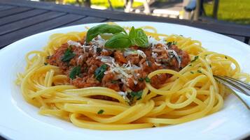 A plate of spaghetti with meat sauce and cheese, garnished with basil, on a white plate.