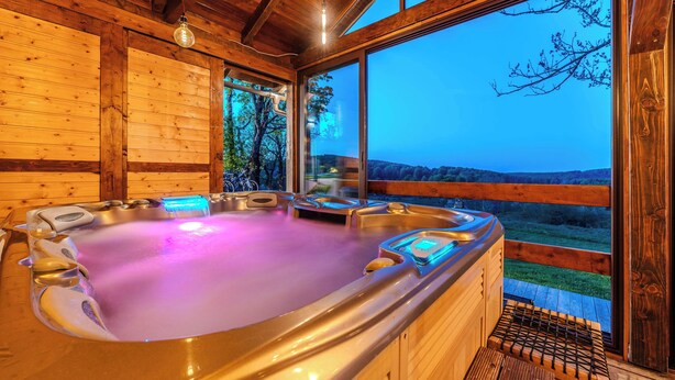 Un espacio de spa de madera con un jacuzzi, paredes de madera y ventanas amplias que ofrecen vistas al paisaje.