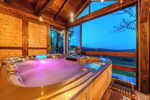 Un espacio de spa de madera con un jacuzzi, paredes de madera y ventanas amplias que ofrecen vistas al paisaje.