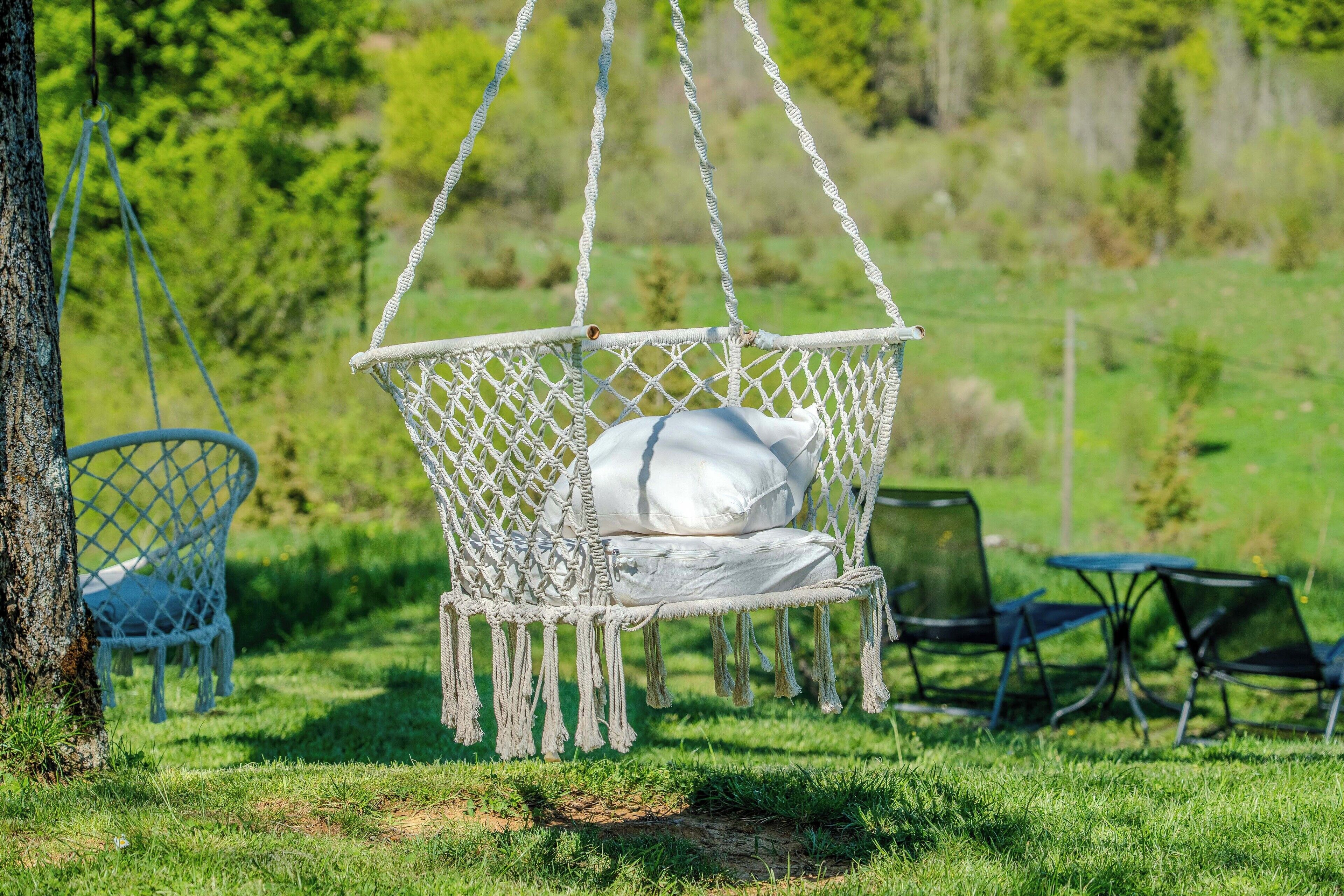 A hammock chair with white cushions in a grassy outdoor area.