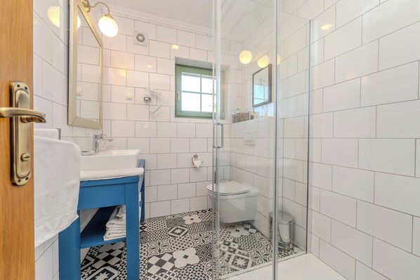 Un baño moderno con azulejos blancos, cabina de ducha de vidrio, tocador azul y baldosas de suelo estampadas.
