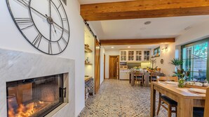 Una cocina acogedora con un reloj grande, una chimenea y un comedor con una mesa preparada para dos.