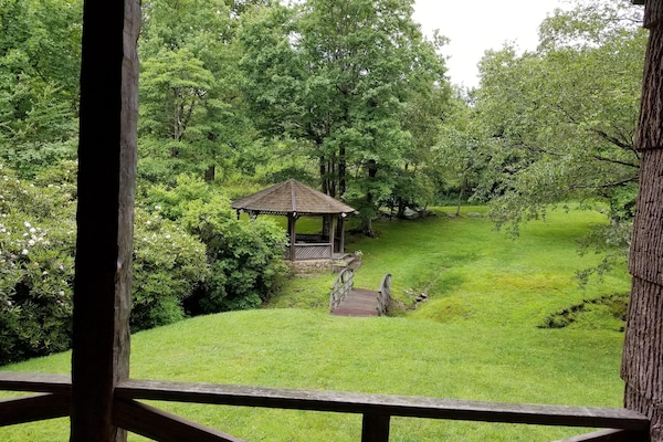 View from covered porch of bridge crossing creek to gazebo, pond and fire pit.