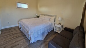 Un dormitorio con cama, mesitas de noche, lámpara, ventana y sofá.