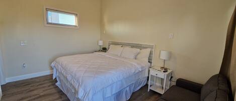 A bedroom with a bed, bedside tables, a lamp, a window, and a sofa.