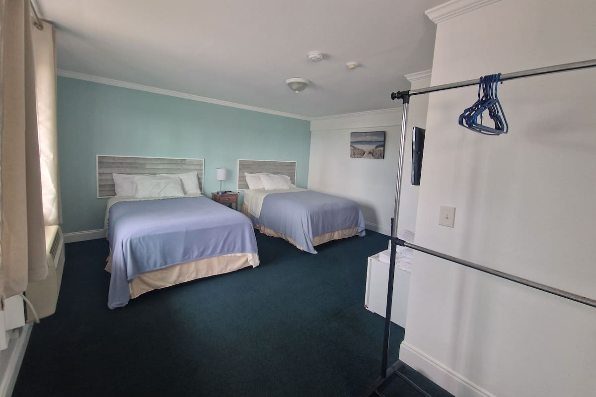 A hotel room with two beds, a TV, a ceiling fan, and a painting on the wall.