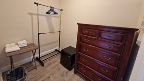 Una habitación con un aparador de madera, un perchero metálico, una mesita con toallas dobladas y un cubo de basura.