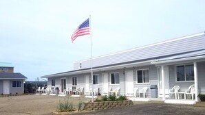 Un motel con asta de bandera, fachada blanca y área de estar al aire libre.