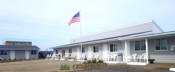 A motel with a flagpole, white exterior, and outdoor seating area.