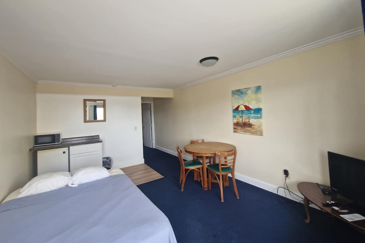 A hotel room with a bed, a desk with a microwave, a chair, a small table, and a TV.