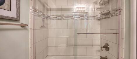 Una ducha moderna con puertas de vidrio transparente, paredes de azulejos blancos y un diseño minimalista.