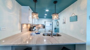 A modern kitchen with a marble countertop, stainless steel sink, and pendant lights.