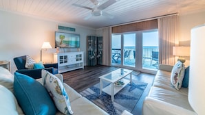 A living room with a white ceiling fan, a sofa, a coffee table, and a view of the outside balcony.