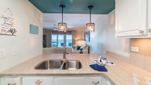 A modern kitchen with a double sink, pendant lights, and a view to the living area.