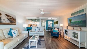 A spacious living room with a white ceiling fan, a beige sofa, a blue armchair, and a white coffee table.