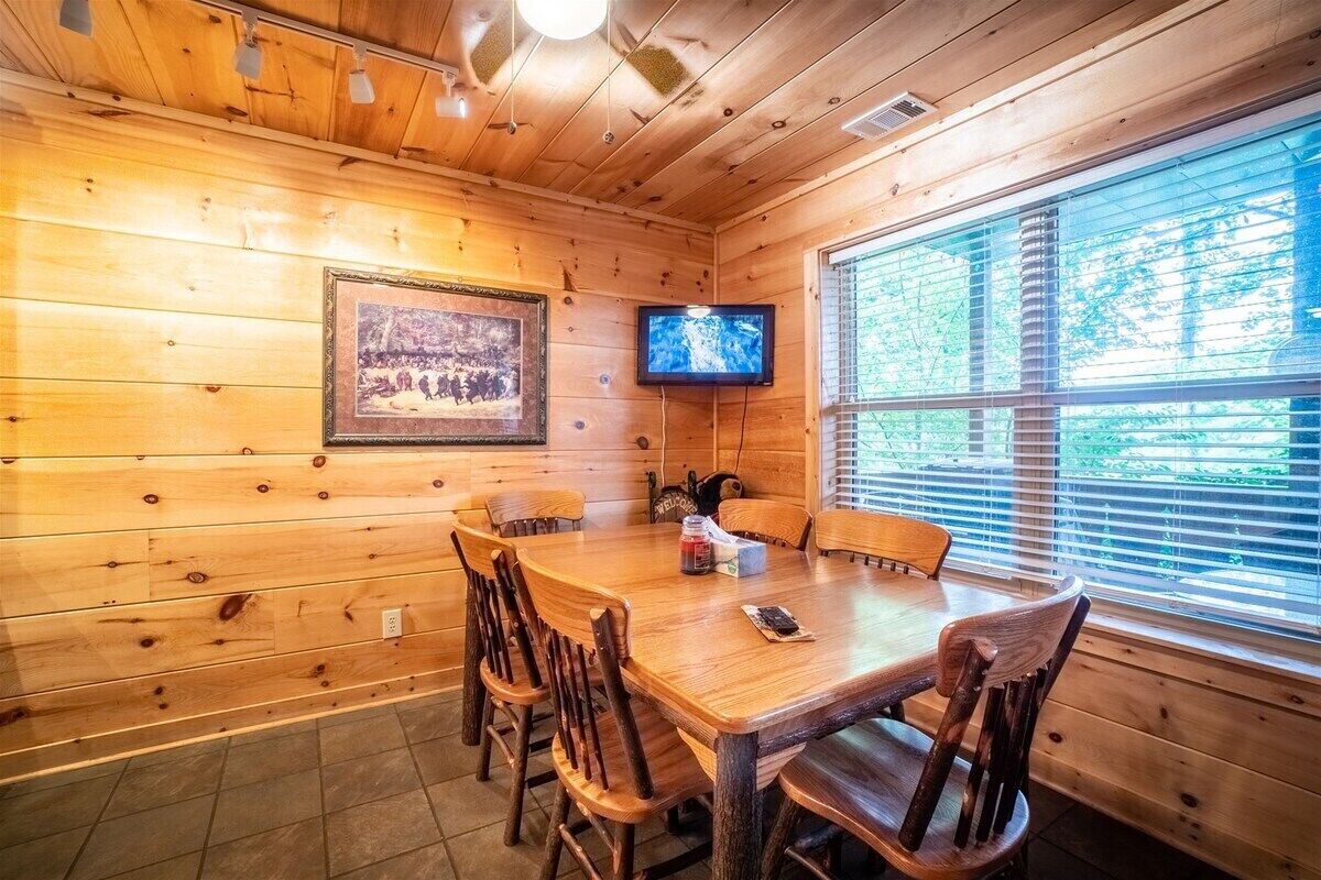 A wooden interior with a dining table, chairs, a television, and a framed picture on the wall.