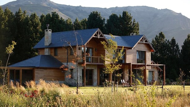 Une maison en bois à deux étages, avec un toit en pente, une cheminée et un balcon.