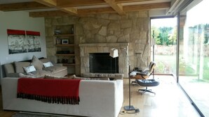 Un salon avec une cheminée en pierre, un canapé agrémenté d’un plaid rouge et un fauteuil.