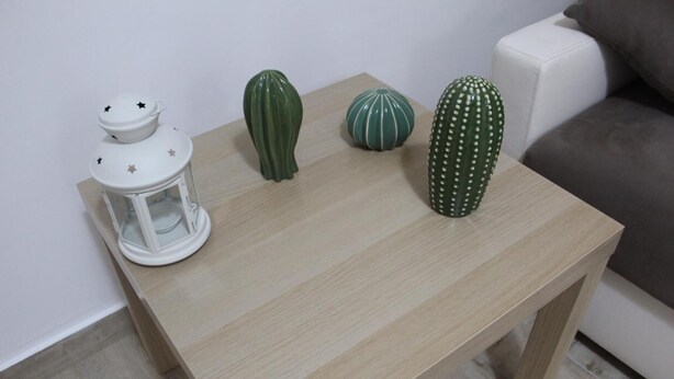 Una pequeña mesa de madera con tres cactus decorativos y un farol blanco.