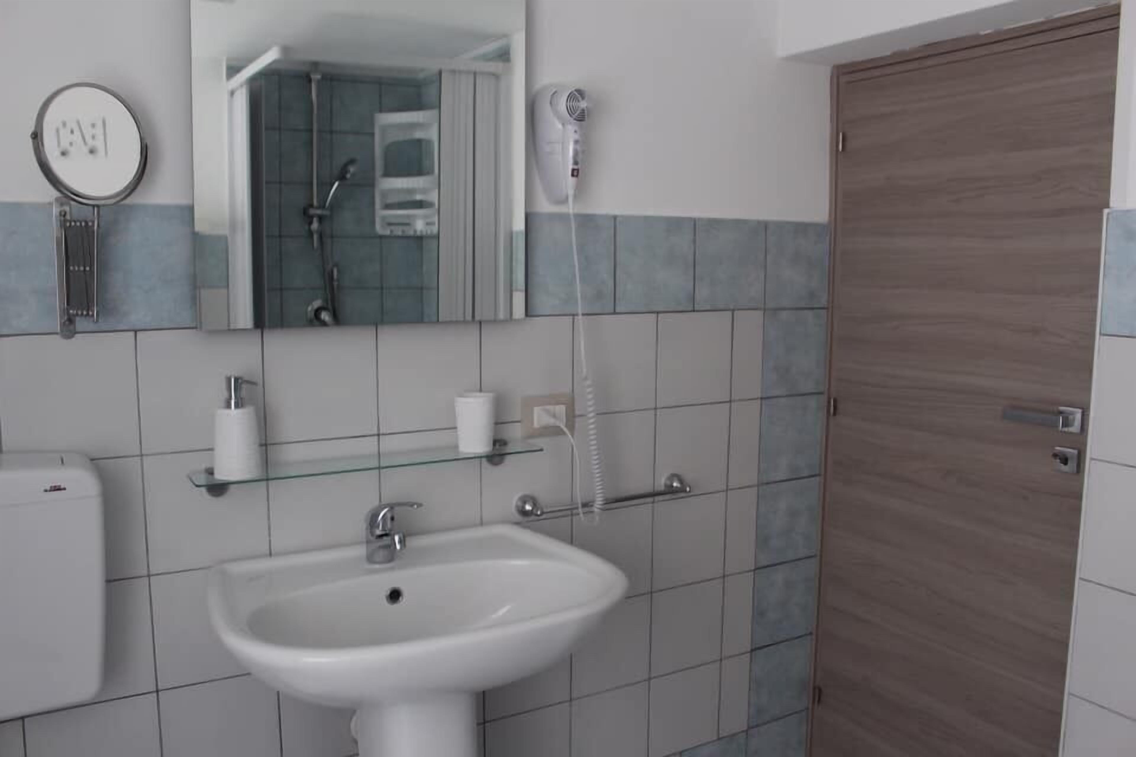 A bathroom with a white sink, a glass shelf with toiletries, a mirror, and a shower area.