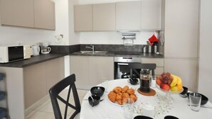 A modern kitchen with a dining area. It includes a microwave, coffee maker, sink, and a table set with croissants, fruit, and coffee. - Kensington by Interhome (La Croix-Valmer)