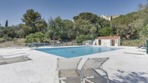 A swimming pool with lounge chairs, surrounded by trees and a hill with buildings in the background. - Kensington by Interhome (La Croix-Valmer)