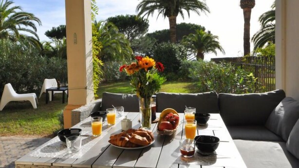 A breakfast setup with a table, seating, and a view of a garden with palm trees and a tower. - Kensington by Interhome (La Croix-Valmer)